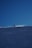 A snowboarder is gliding down a snowy slope under a clear blue sky. The person is wearing a red jacket and appears to be skillfully maneuvering on the snow. The snow is sparkling in the sunlight, creating a dynamic and energetic scene.
