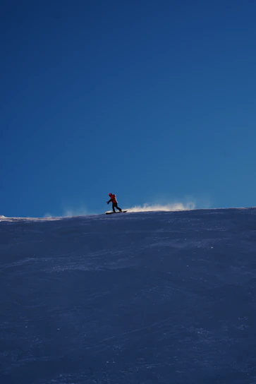 A snowboarder cruising down a snowy hill with a Chug Chariot strapped securely, cans gleaming in the sun.