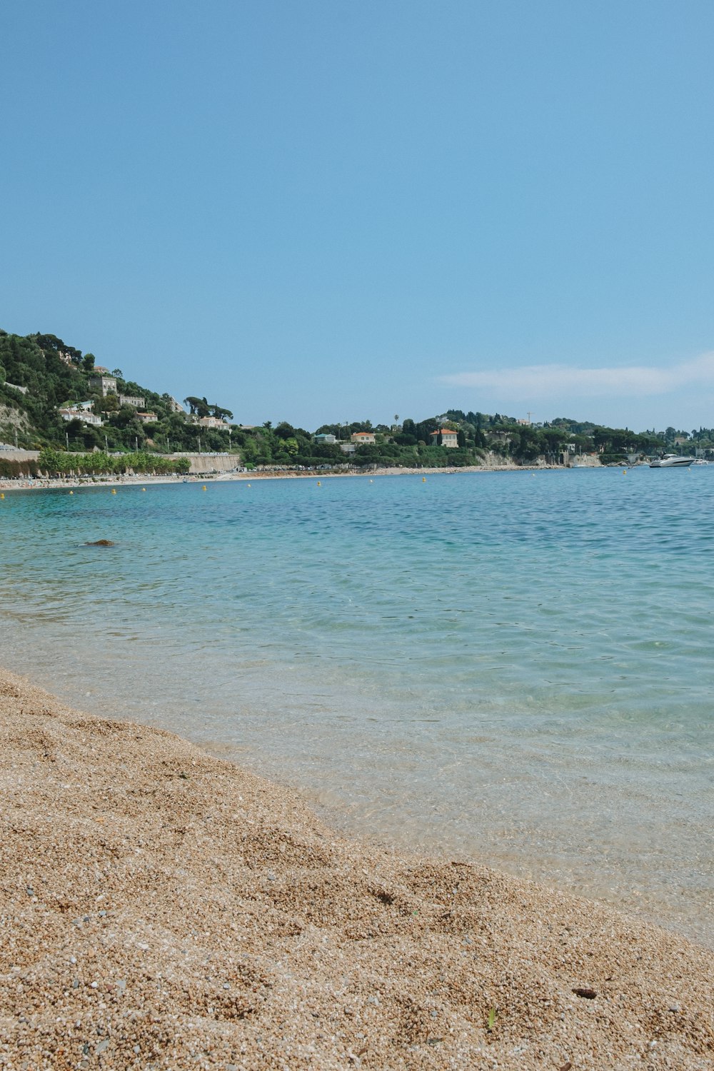 a sandy beach with clear blue water and a hill in the background