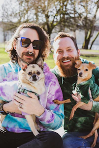 dos hombres sonriendo con perros pequeños en mano