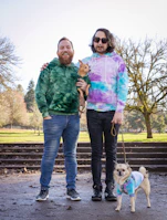 Two dogs playing outdoors, one dressed in a vibrant blue hoodie and the other in a patterned bandana.