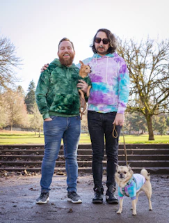 Two dogs of different sizes showing off their matching custom hoodies in a park.