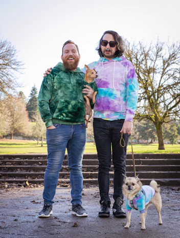 Two playful dogs dressed in vibrant matching hoodies, enjoying a sunny park.