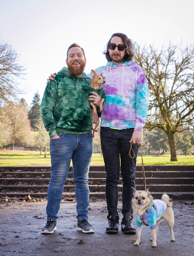 A happy dog and cat duo wearing matching bright hoodies, playing together in a colorful park.