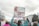 A group of people participating in a protest or march. One person in the foreground is holding a large sign with an image of a fetus and a pair of forceps, alongside the text 'FORCEPS OFF their bodies! RehumanizeIntl'. Other signs in the background include phrases like 'STOP CALLING VIOLENCE FEMINISM'. The participants are surrounded by trees and a building with an American flag.