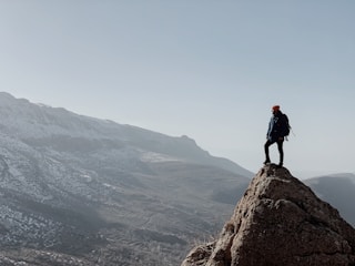 Hiker standing triumphantly at Toubkal summit with panoramic mountain views