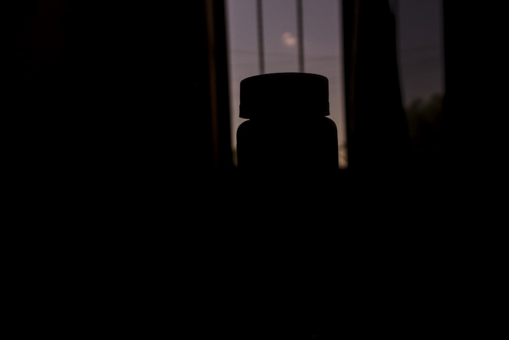 Una botella sentada frente a una ventana en una habitación oscura