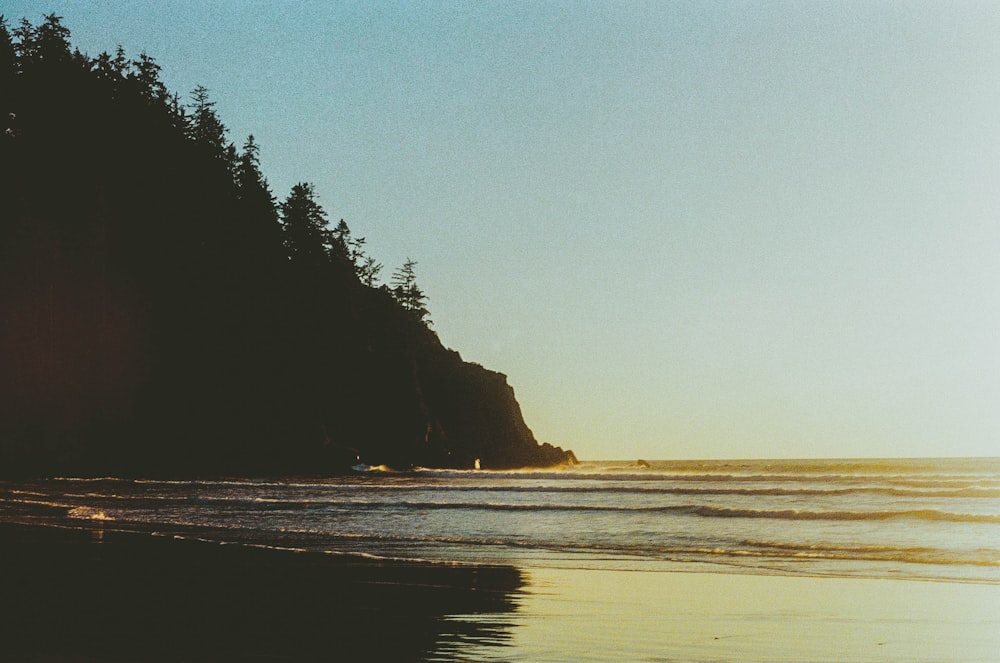 the sun is setting on a beach with a boat in the water