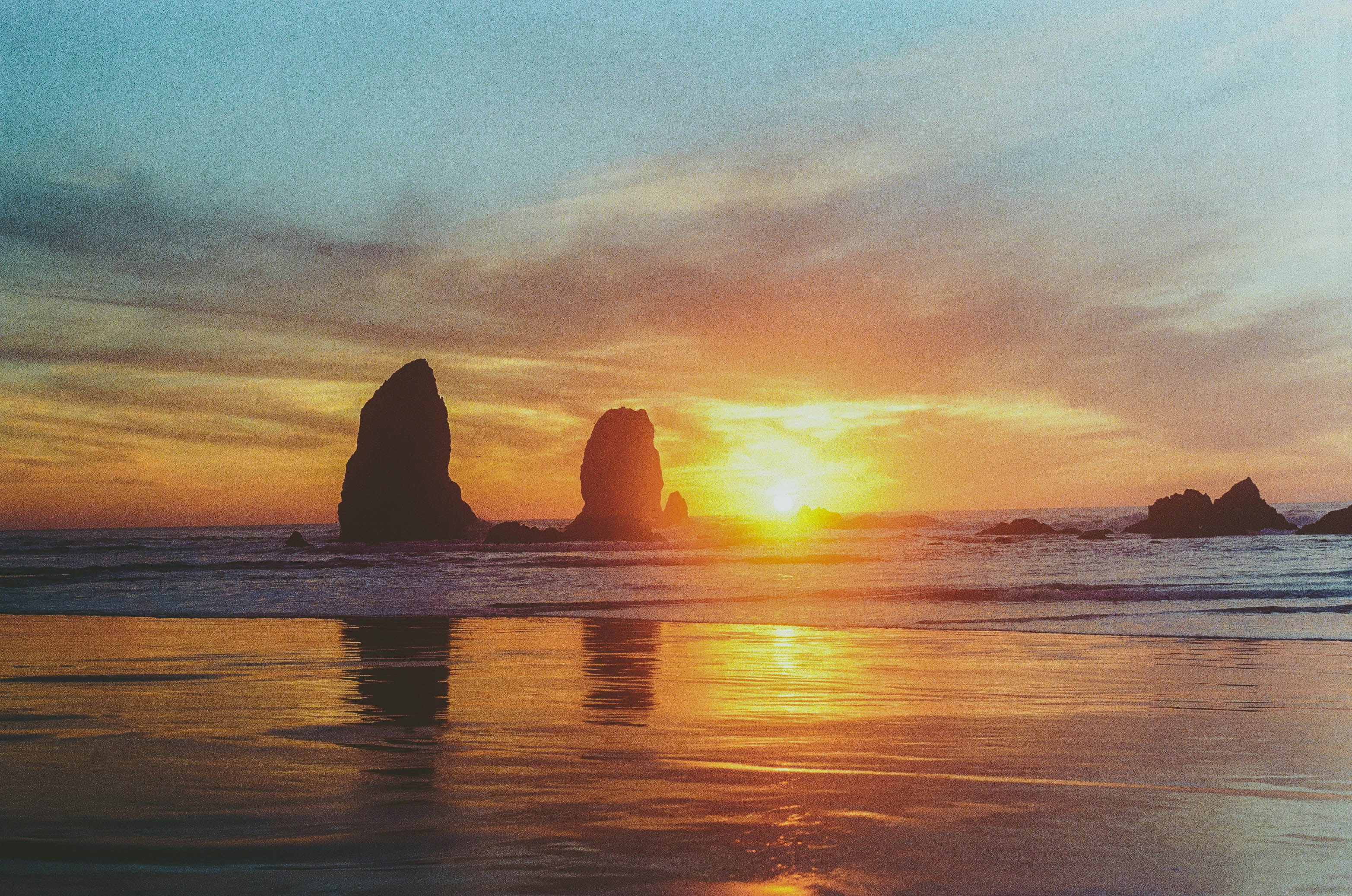 the sun is setting over the ocean with rocks in the water, 