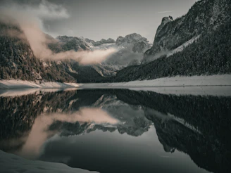 A serene mountain lake reflecting snow-capped peaks at dawn with mist hovering above the water