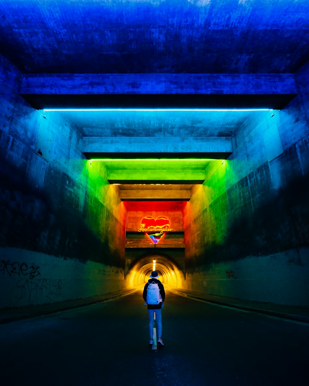 a person standing in a tunnel with a rainbow light