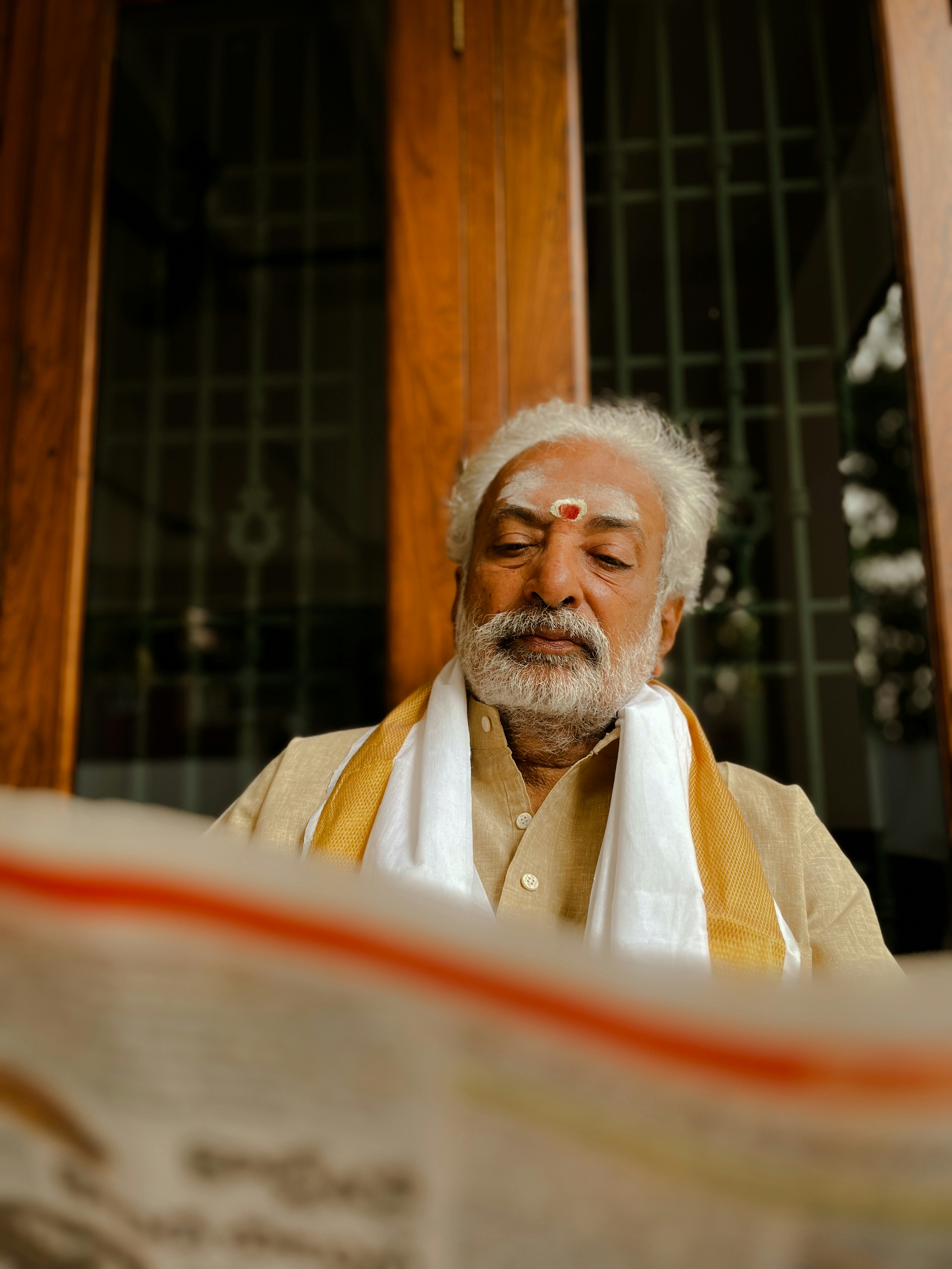 Elderly North Indian man with white hair and glasses wearing white kurta standing proudly in front of well-organized kirana store