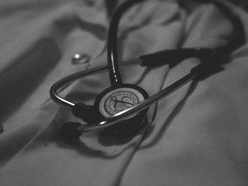A sleek dark navy background with gold accents framing a vintage medical stethoscope resting on an open notebook.