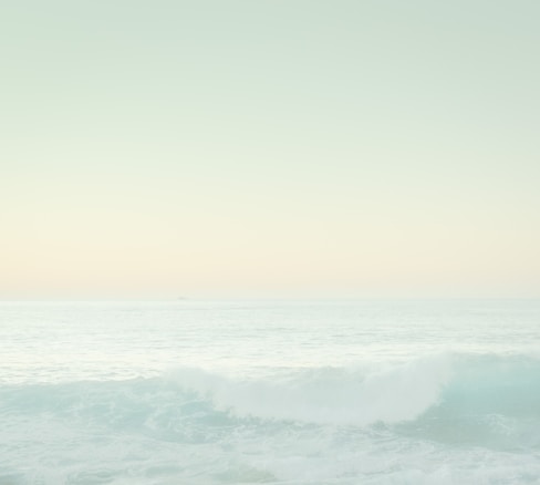 A serene ocean view with gentle waves and a pastel sky. The light creates a soothing gradient from the horizon line, blending softly into the sea.