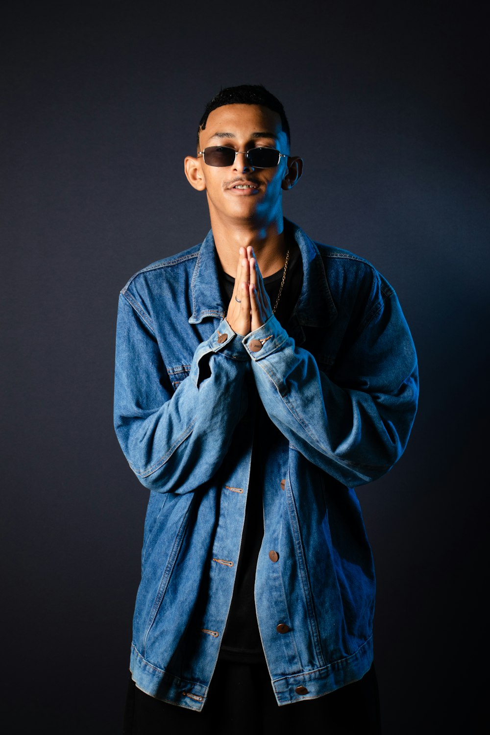 a man in a denim jacket and sunglasses standing in front of a black background