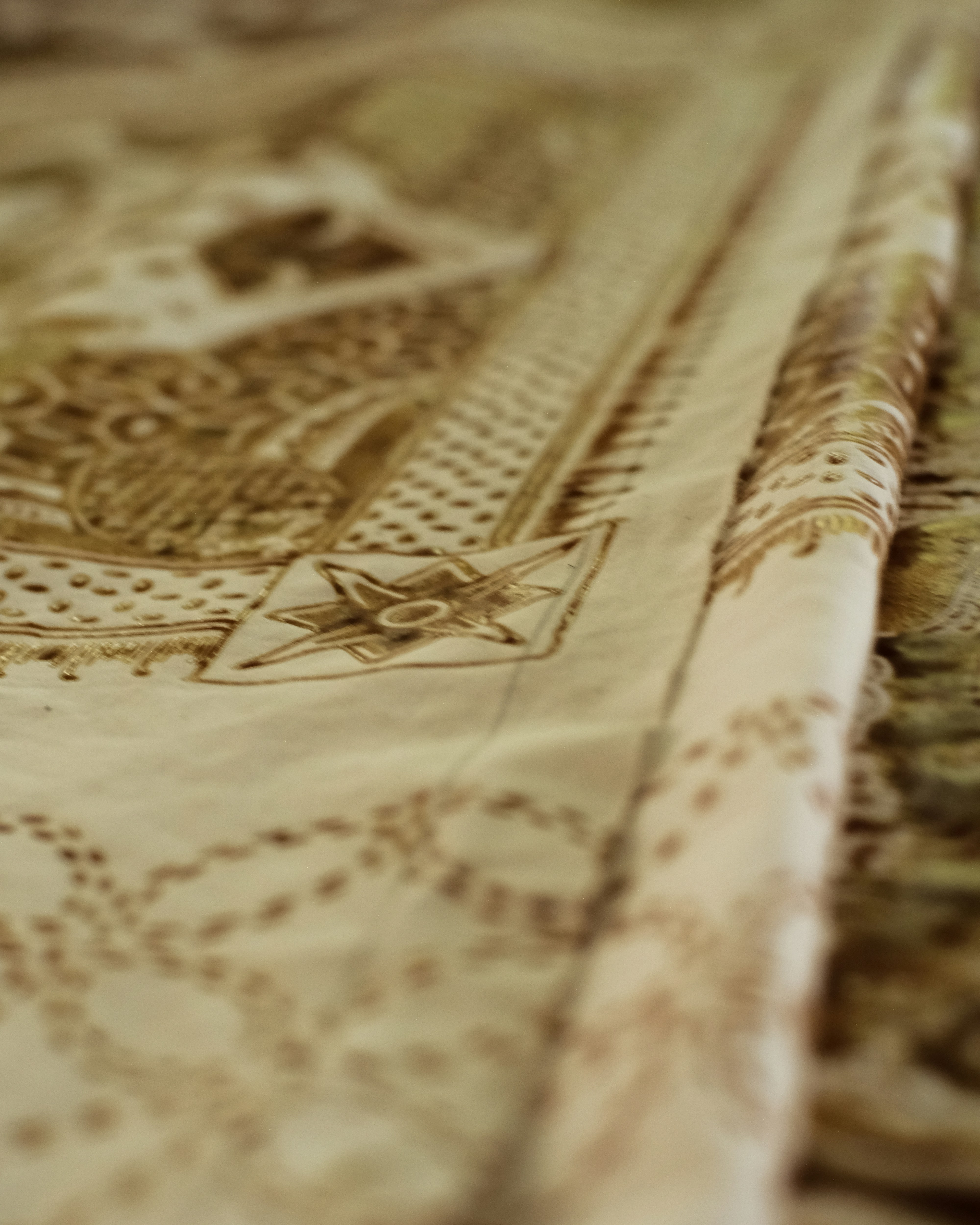 Close-up of delicate hand embroidery with gold thread on ivory silk fabric