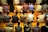 A group of people are sitting on prayer mats in a place of worship. They are positioned closely together in multiple rows facing the same direction. The setting suggests that they are engaged in a communal prayer session.