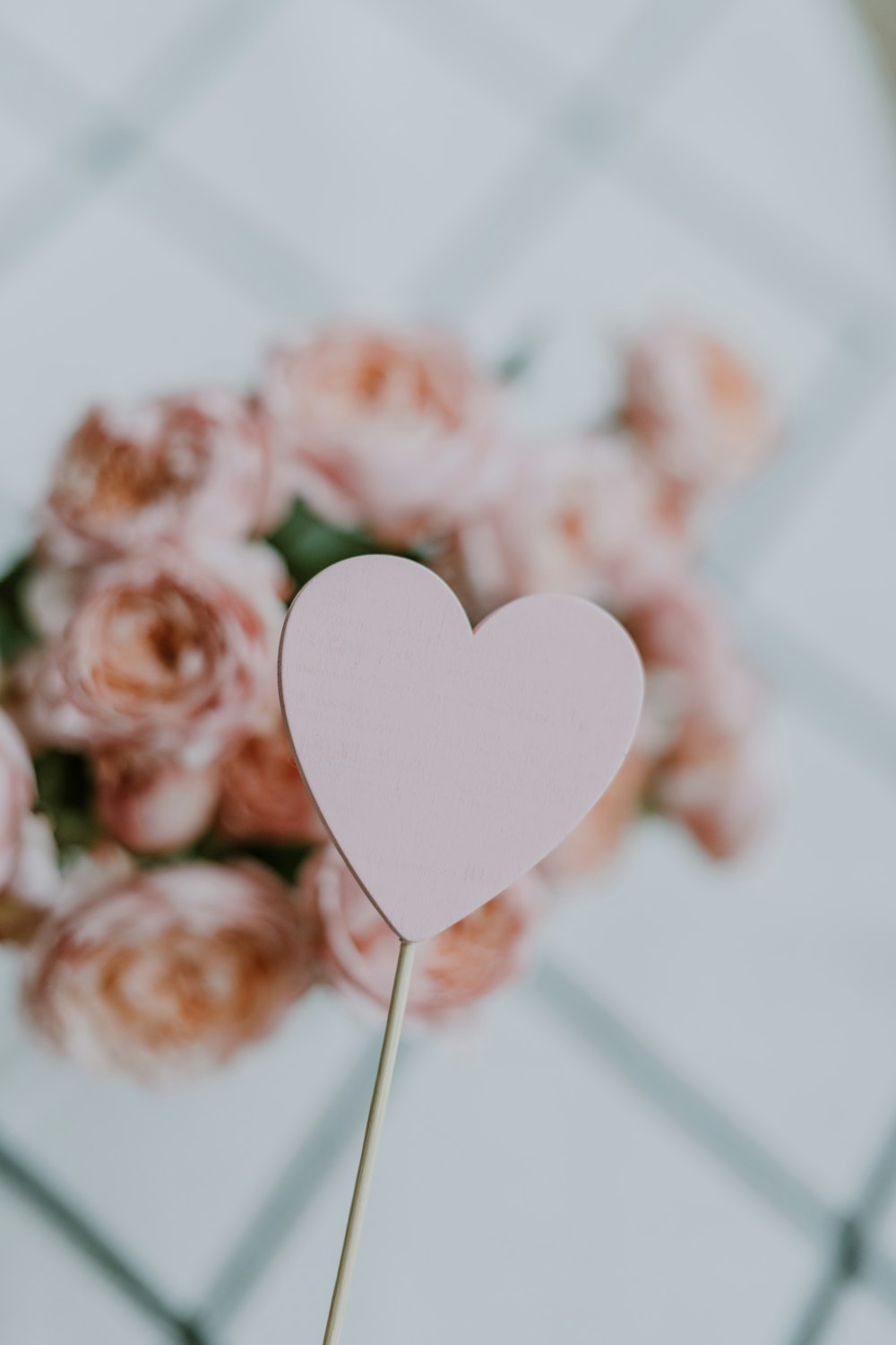 a pink heart on a stick in front of a bouquet of pink roses