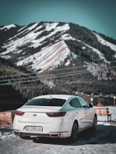 A sleek white Innova Crysta parked against a backdrop of snow-capped Himalayan peaks under a clear blue sky.