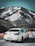 A happy family standing beside a white Innova Crysta with snow-capped mountains in the background.