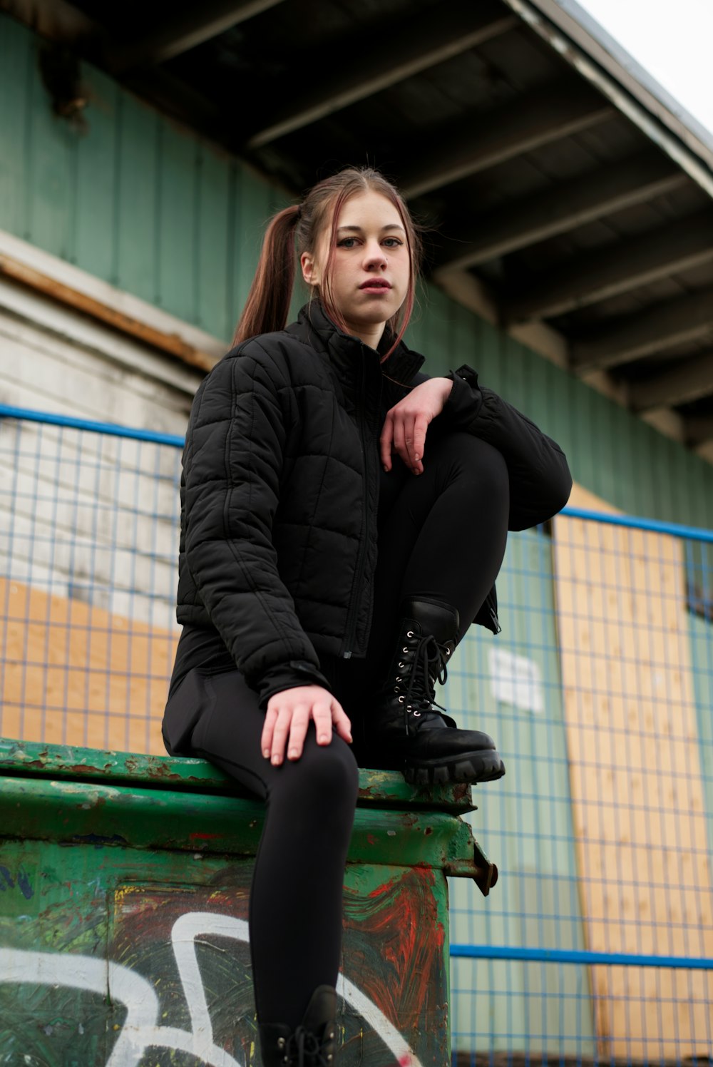 a woman sitting on top of a green trash can