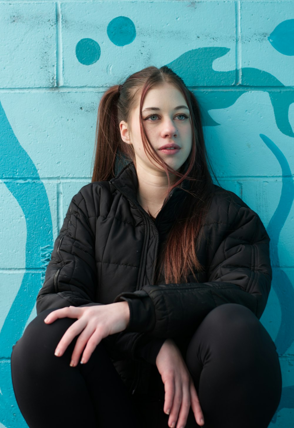 a woman sitting against a blue wall with her hands on her knees