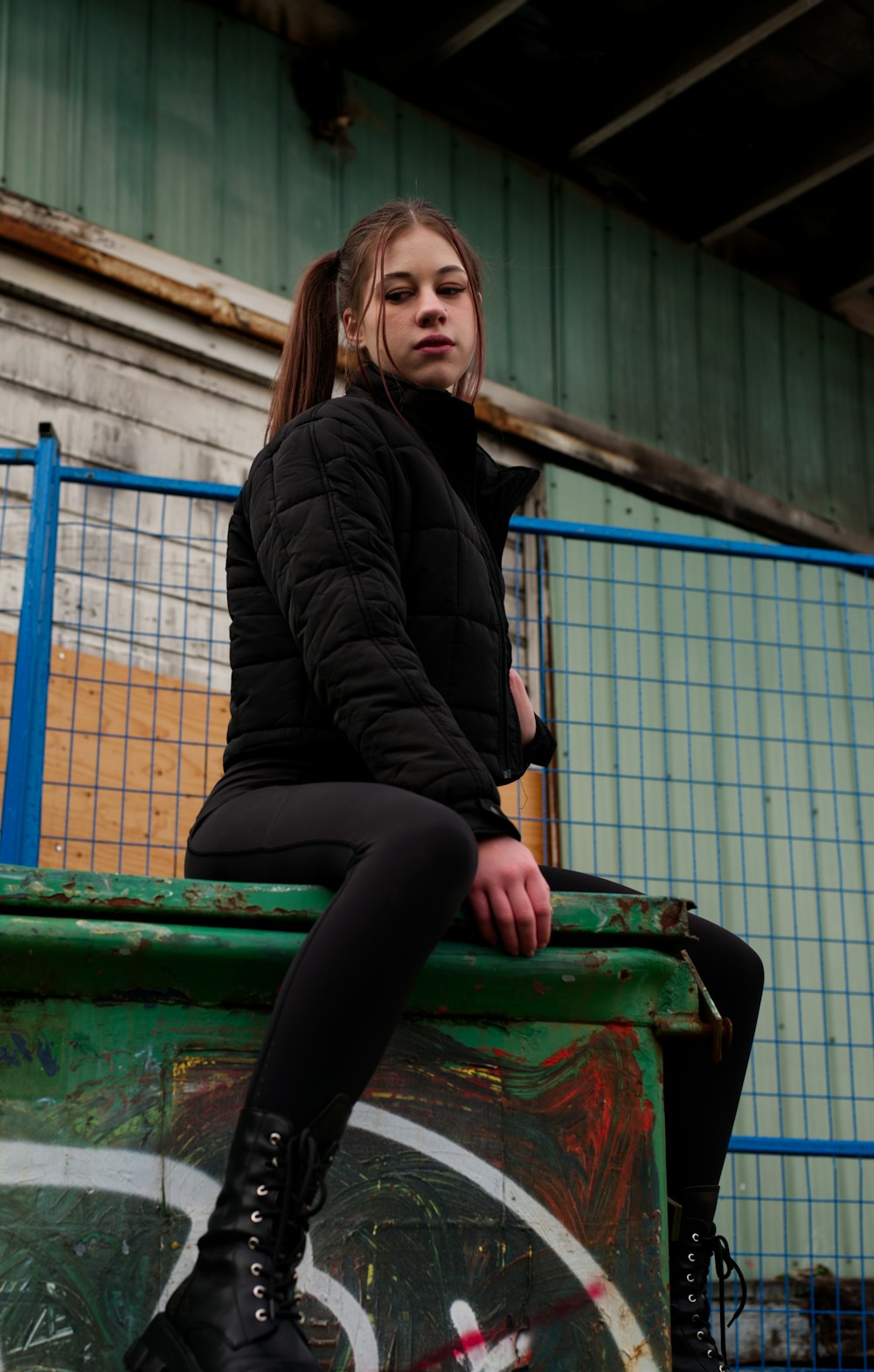 a woman sitting on top of a green trash can