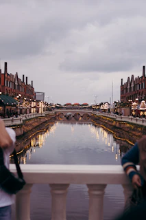 two people standing on a bridge looking at a canal