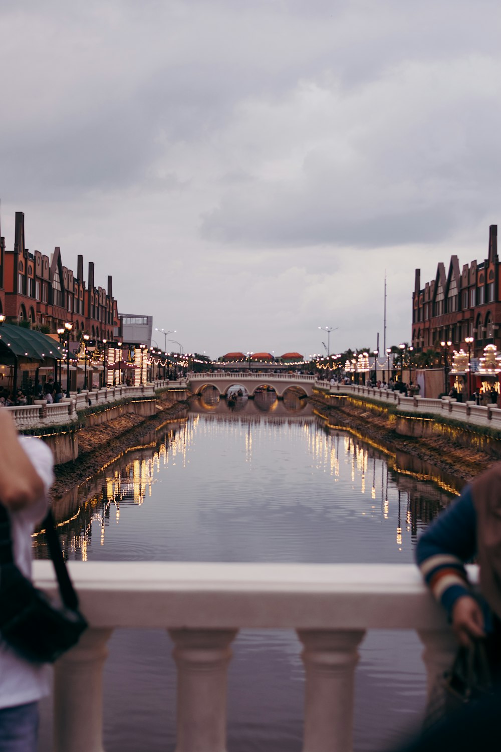 two people standing on a bridge looking at a canal