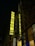 A tall building displays a vibrant, illuminated sign with the word 'FABRIKA' and 'HOSTEL' vertically aligned. The sign is bright yellow, set against a dark night background. The surrounding structure features large windows and a detailed decorative facade.