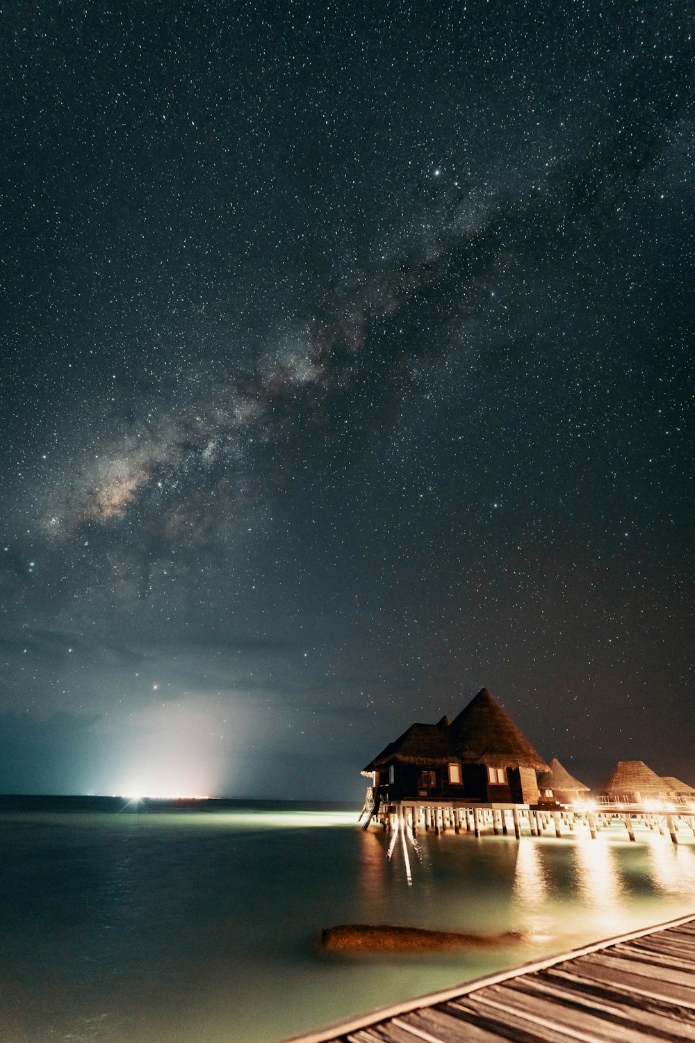 the night sky over the water and a wooden pier