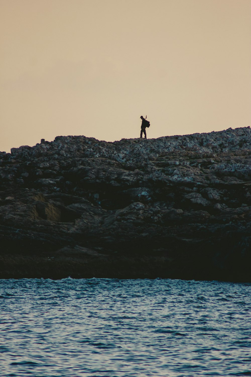 a person standing on top of a rocky hill next to a body of water