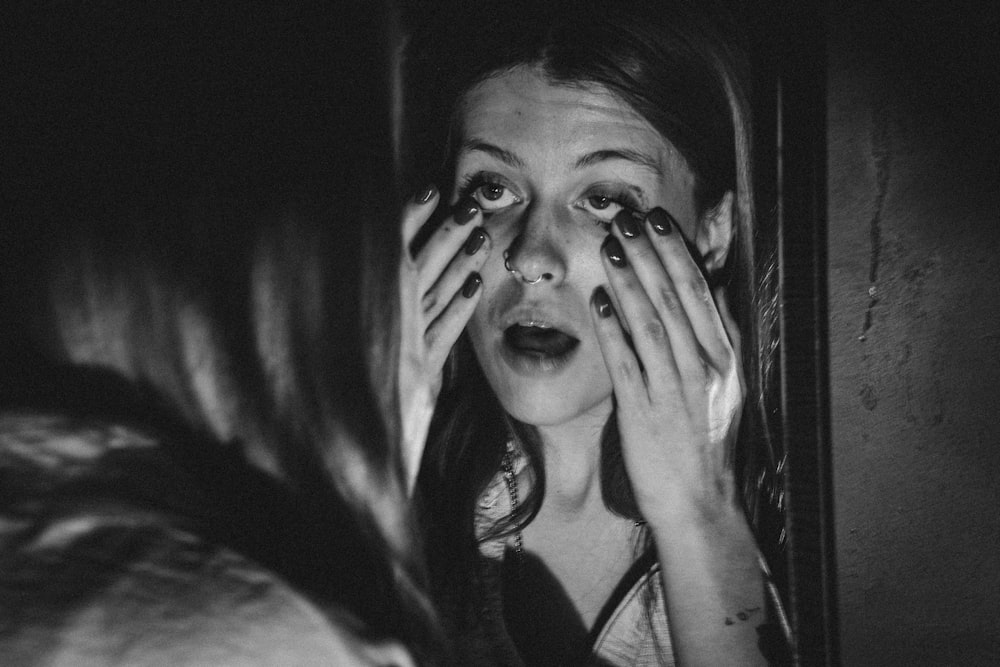 a woman covering her eyes in front of a mirror