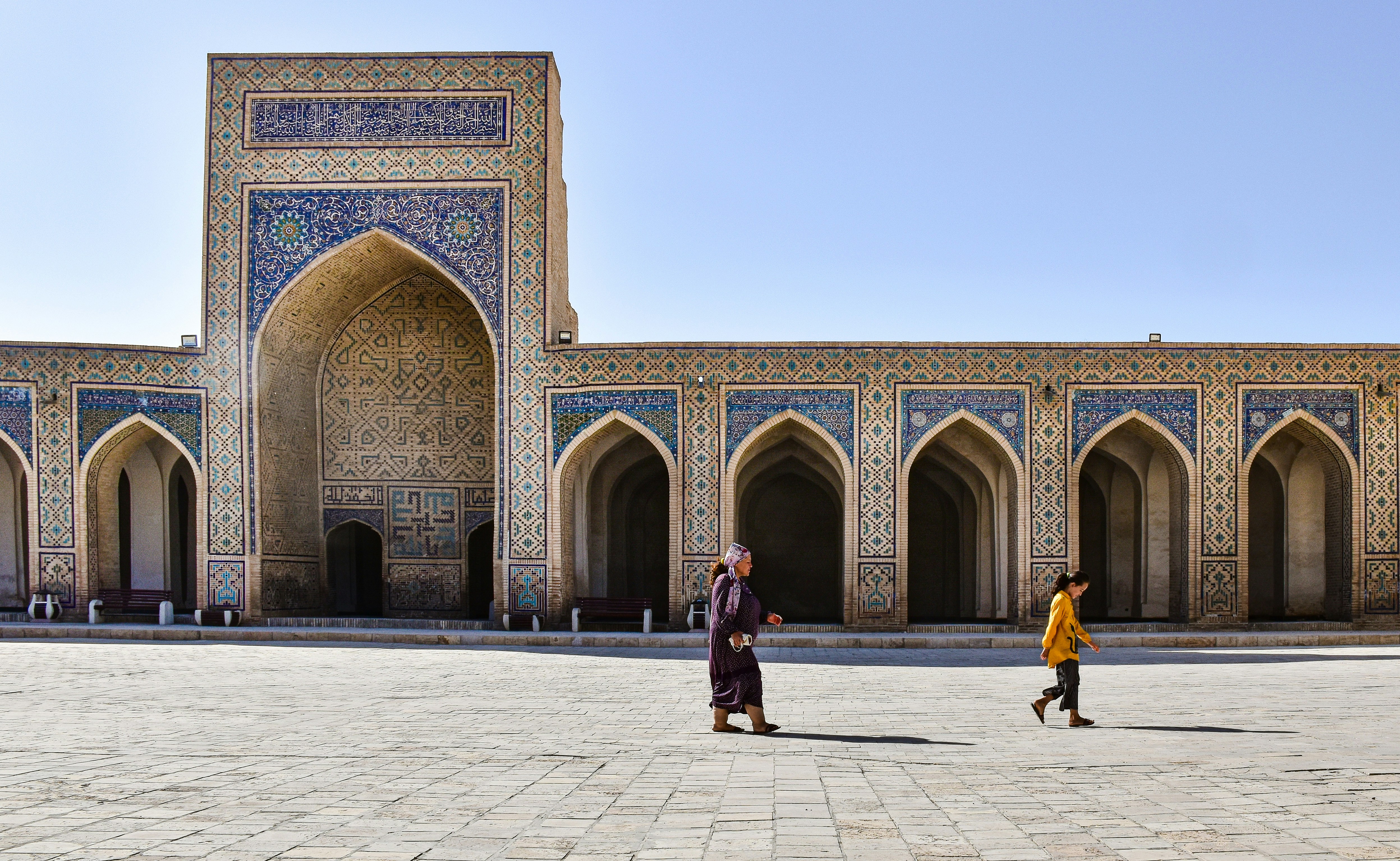 two people walking in front of a building, Bukhara, Uzbekistan.