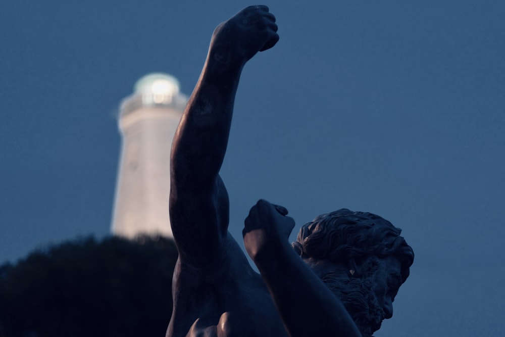 a statue of a person holding a light house in the background