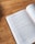An open book featuring text in Arabic is resting on a wooden surface. Natural light illuminates the page, revealing intricate typographic details.