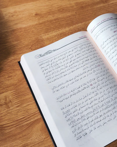A serene photograph of an open Qur’an resting on a wooden table with morning sunlight streaming through a window.