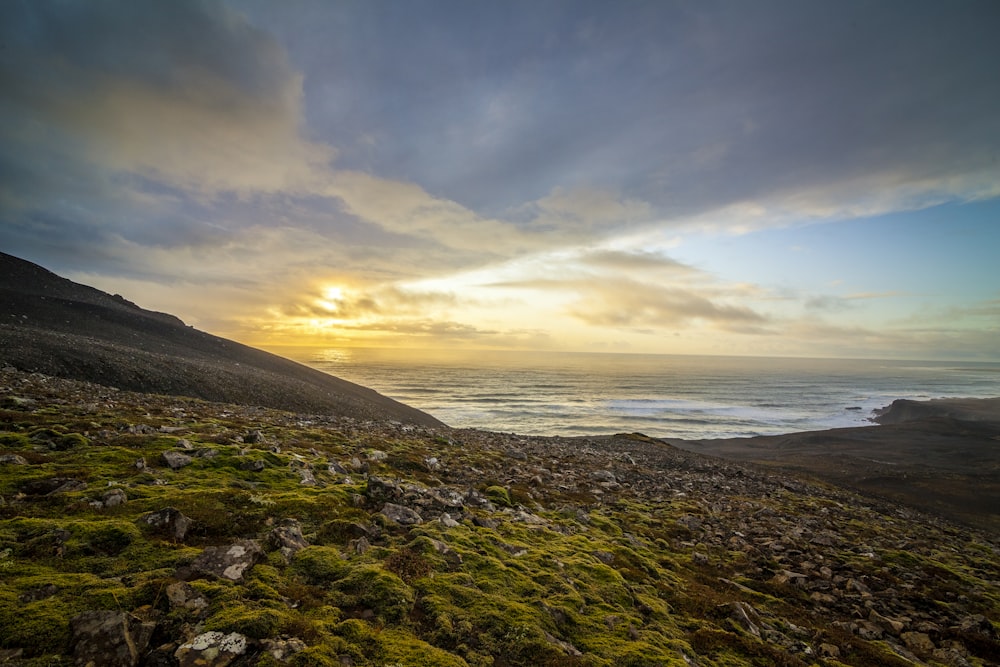 the sun is setting over the ocean on a rocky hillside