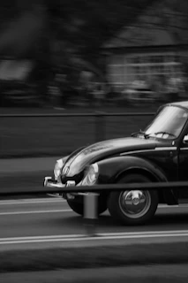 A black-and-white still of a vintage car in motion, emphasizing texture and contrast