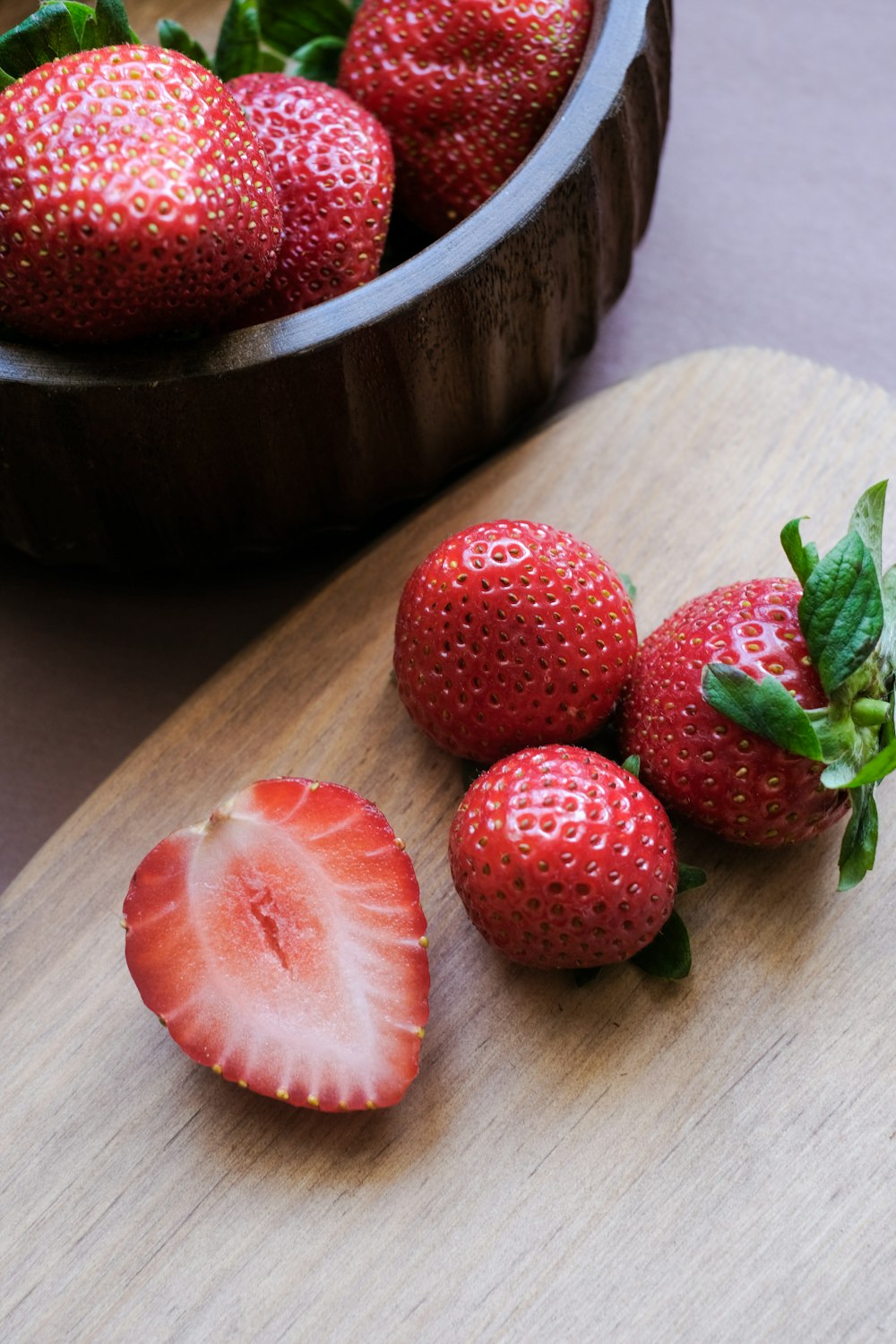 a wooden cutting board topped with a bowl of strawberries