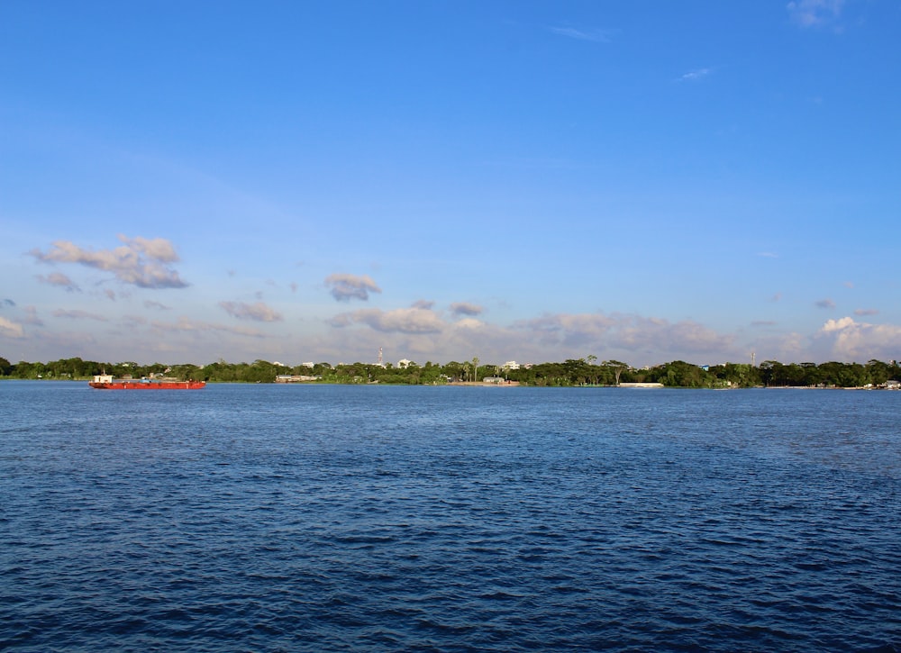 a large body of water with a red boat in the distance