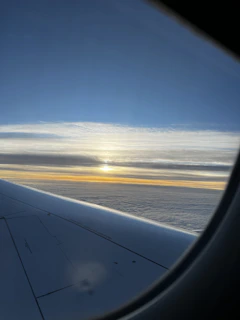 A serene view of a plane flying over a sunset sky with a silhouette of Makkah's skyline below.