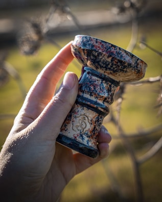 Hand holding a beautifully crafted glass piteira against a blurred background.