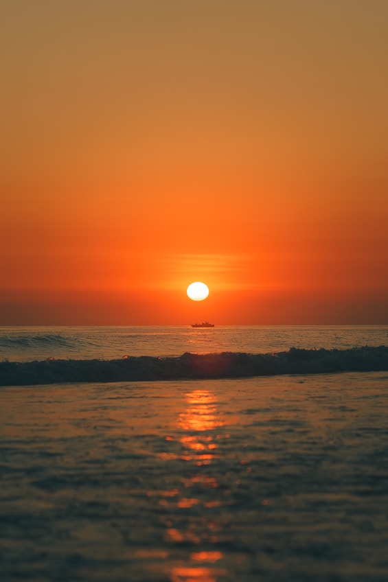 the sun is setting over the ocean with a boat in the distance