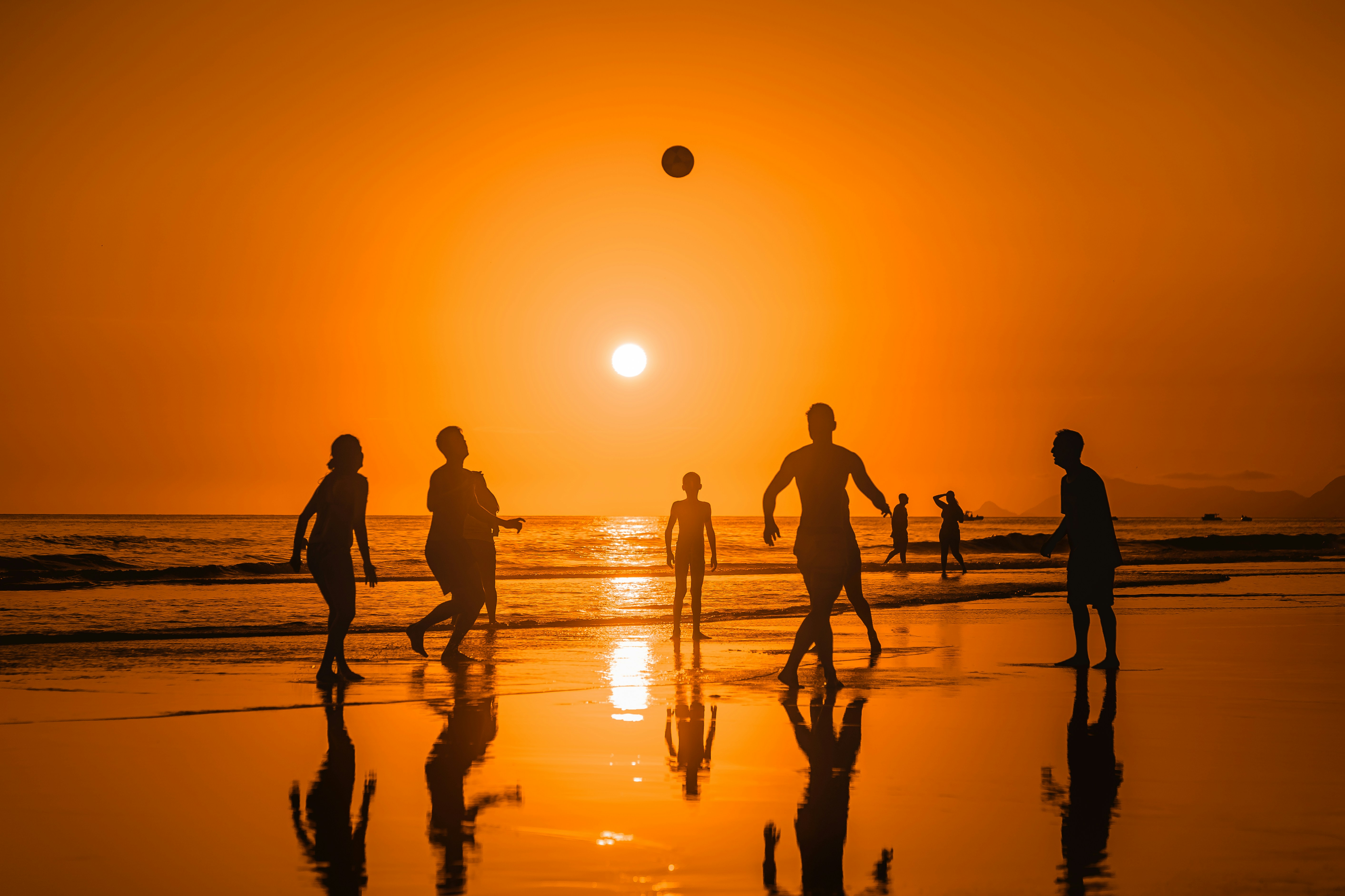 A group of people playing soccer on the beach at sunset