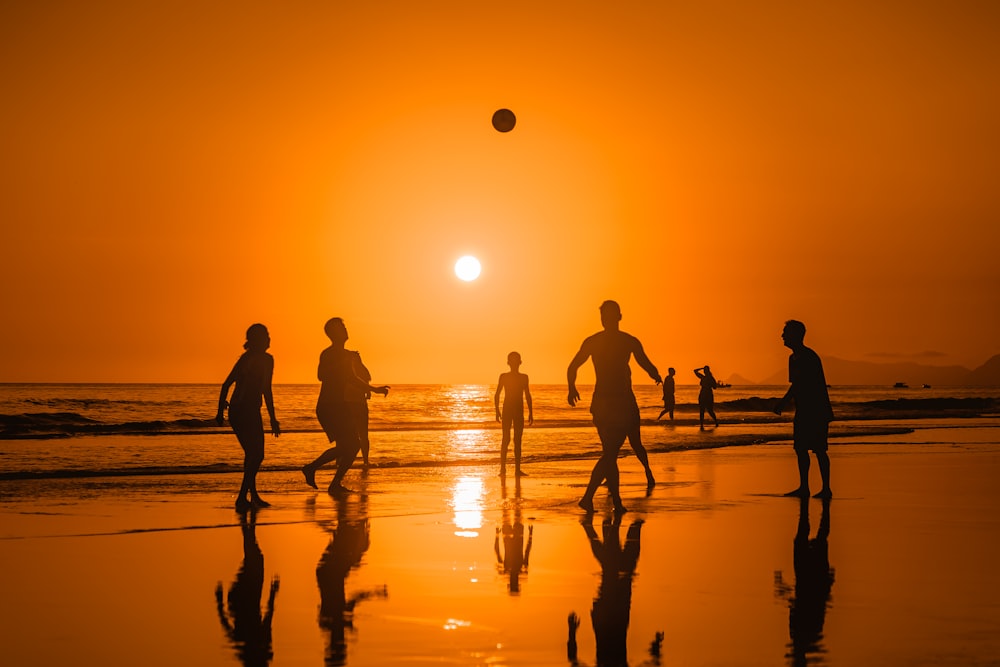 a group of people playing soccer on the beach at sunset