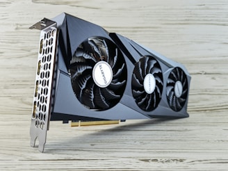 A modern graphics card with two large cooling fans and a sleek, angular design. The metal casing is dark and the fans display a brand name. The card's ports are visible on the left side, with honeycomb ventilation.