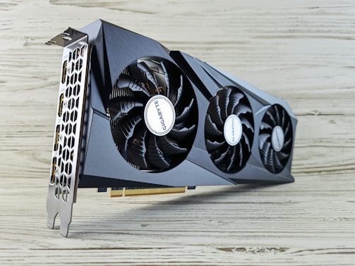 A modern graphics card with two large cooling fans and a sleek, angular design. The metal casing is dark and the fans display a brand name. The card's ports are visible on the left side, with honeycomb ventilation.