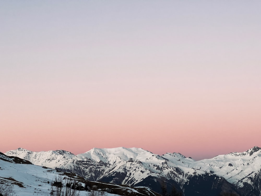 a view of a snowy mountain range with a pink sky