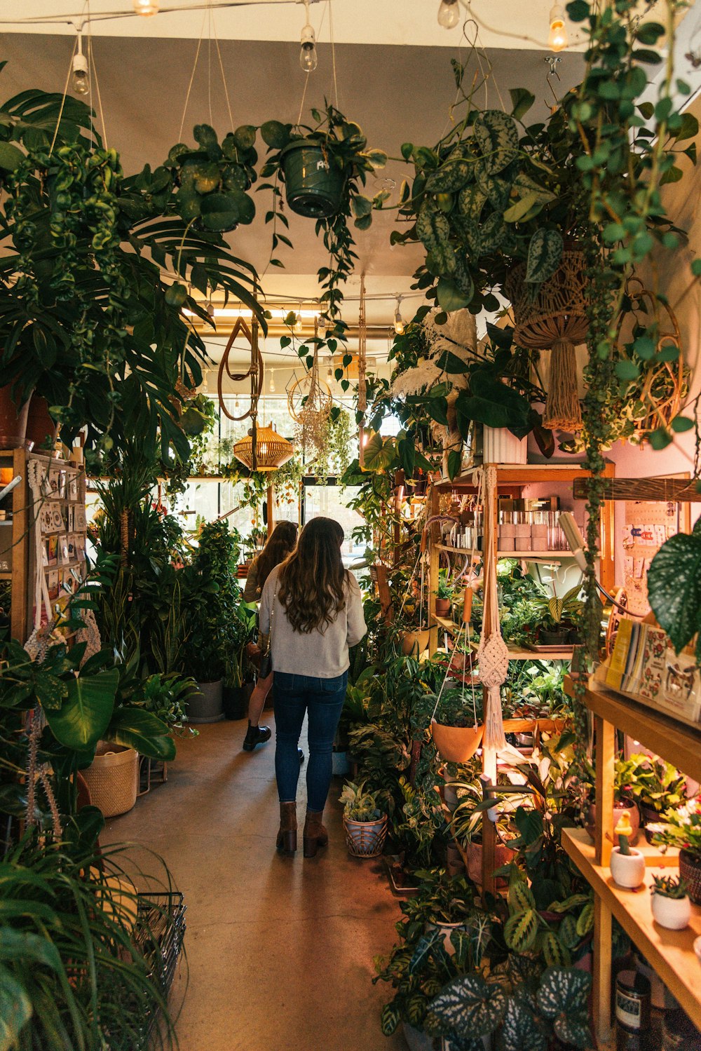 a woman walking through a store filled with lots of plants